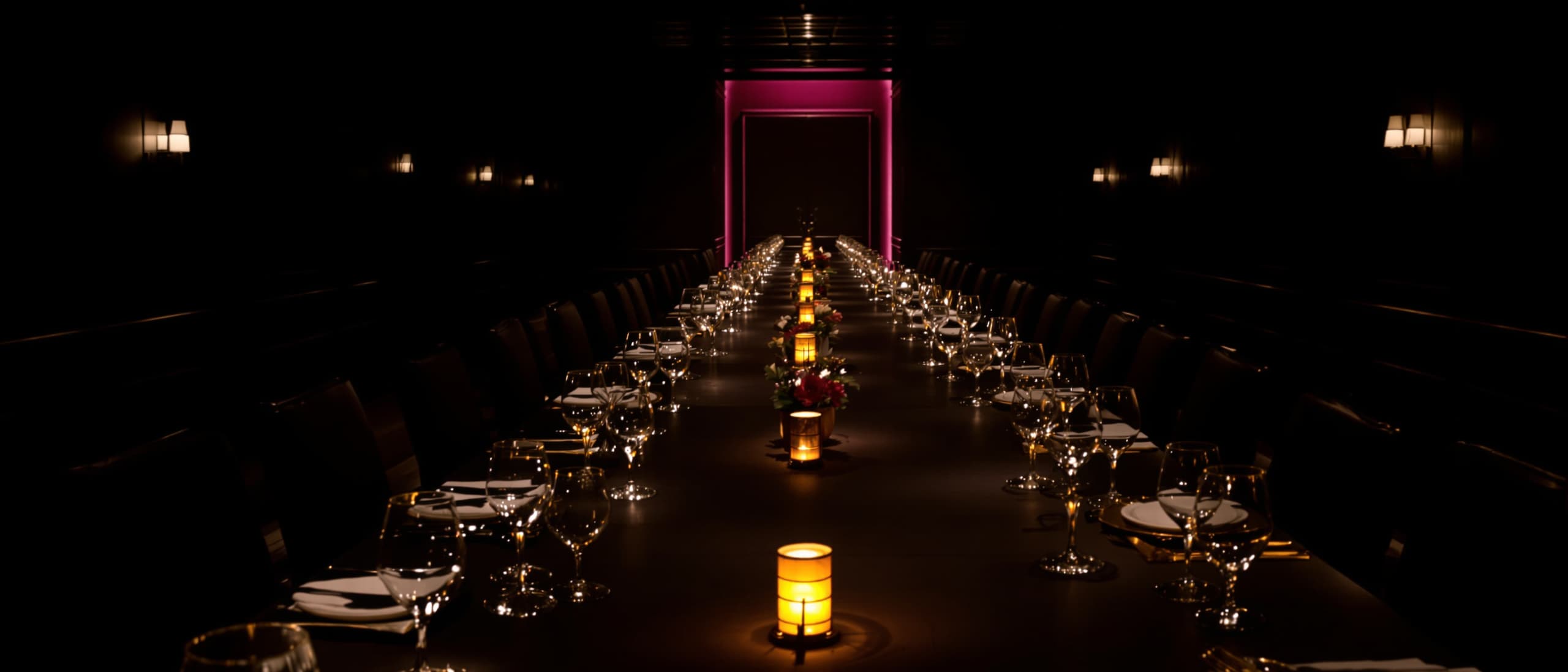 A long dinner table set in a dark private room, waiting for guests