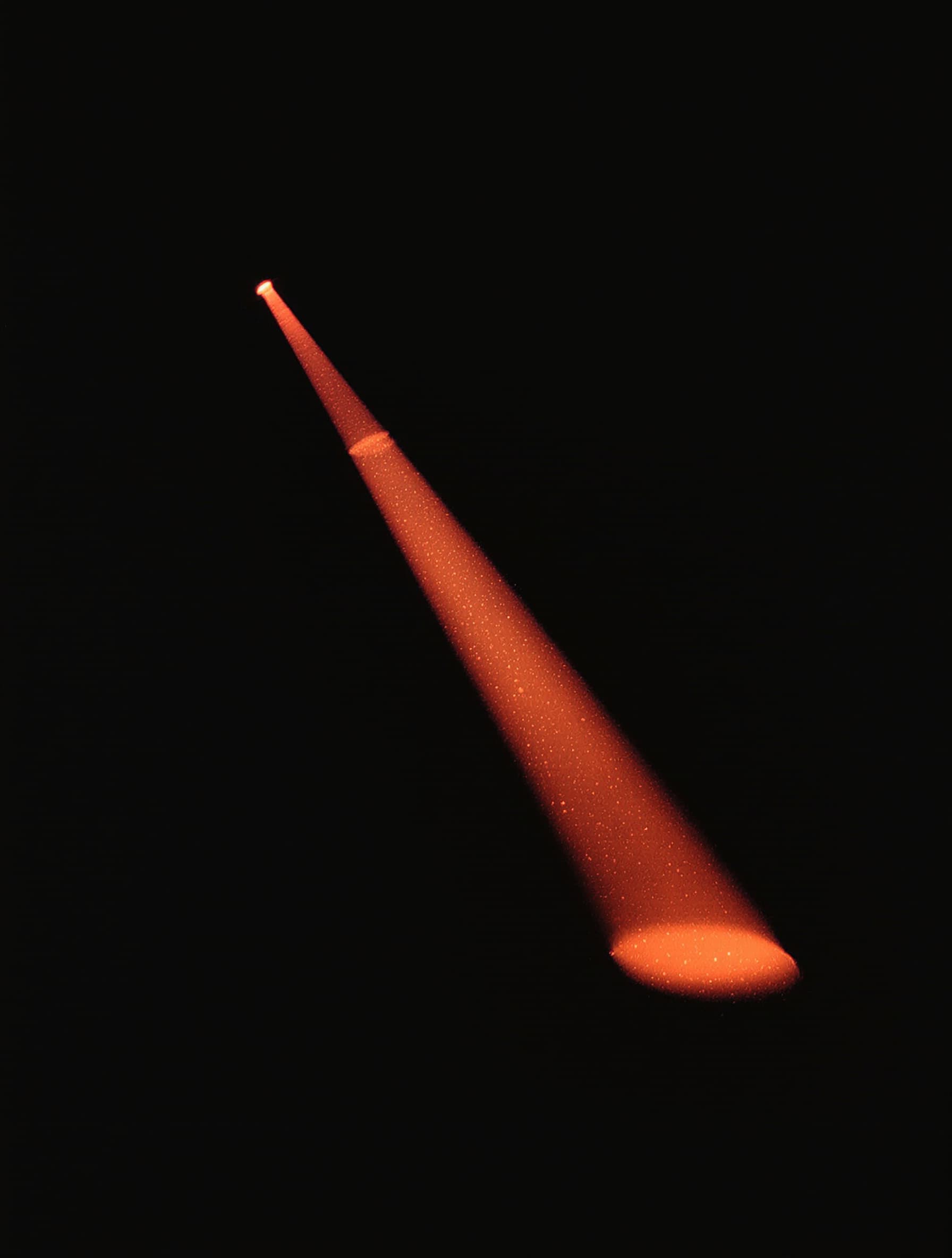 A single beam of coral light cutting through haze in a dark room